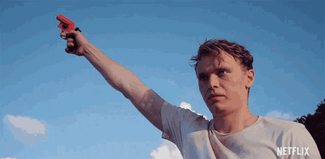 a man in a white shirt is holding a red toy gun with netflix written on the bottom of his shirt