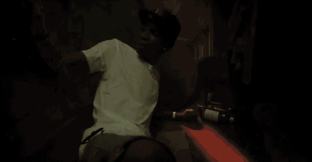 a man in a white shirt is sitting in a dark room with a bottle of beer