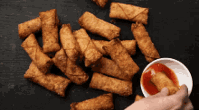 a person is dipping a fried egg roll into a bowl of sauce
