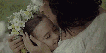 a woman is kissing a little girl on the cheek while the little girl has a flower crown on her head .