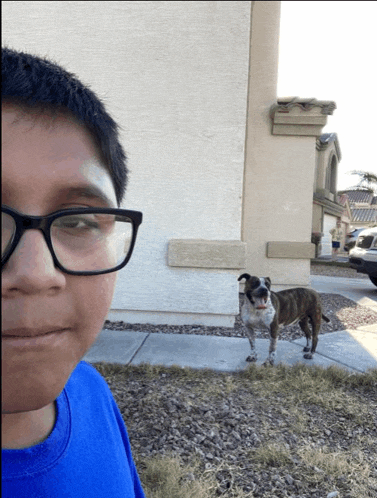 a boy wearing glasses stands in front of a dog