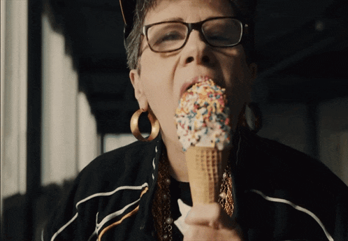 a woman wearing glasses is eating an ice cream cone covered in sprinkles