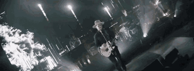 a man in a hat is singing into a microphone while playing a guitar on stage .