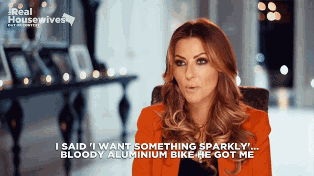 a woman in an orange jacket says " i said i want something sparkly ... bloody aluminium bike he got me "