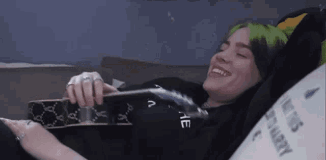 billie eilish is laying on a bed playing a guitar .