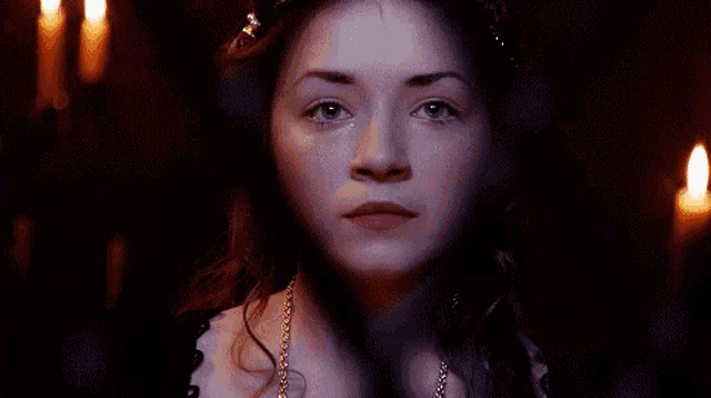 a woman in a dark room with candles behind her