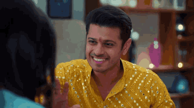 a man wearing a yellow shirt with sequins is smiling
