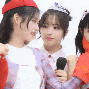 a girl with a tiara on her head holds a microphone while two other girls look on