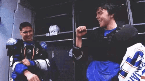 two hockey players are standing in a locker room and one of them is wearing a jersey with the number 34 on it