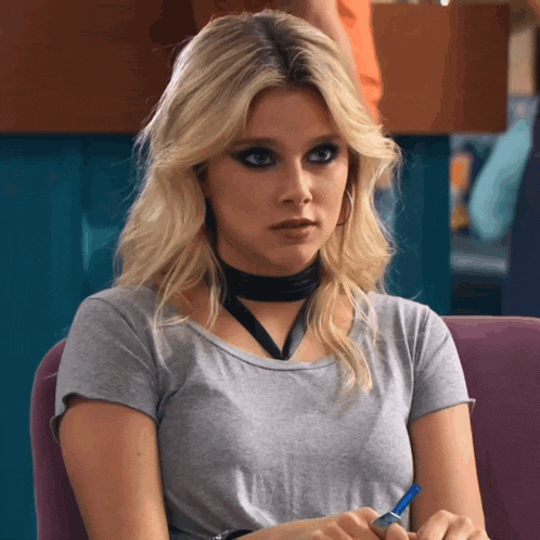 a woman wearing a choker and a grey shirt is sitting in a chair