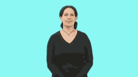 a woman in a black shirt and necklace is standing in front of a blue background and making a hand gesture .
