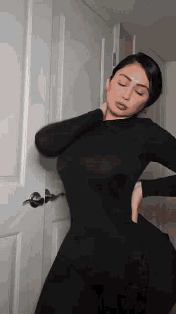a woman in a black bodysuit is standing in front of a door