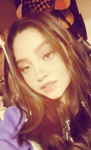 a girl wearing a plaid hat and a purple sweatshirt looks at the camera