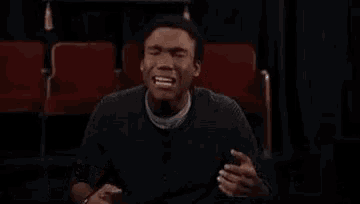 a man is sitting in a theater with his mouth open and the words `` my emotions '' written on the screen behind him .