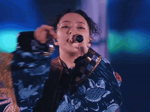 a woman singing into a microphone wearing a blue and gold jacket