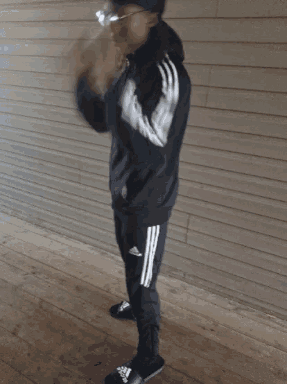 a man wearing a black adidas tracksuit is holding a bottle