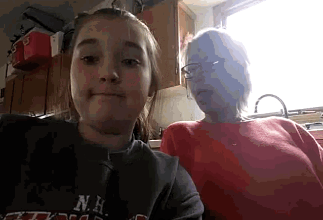 a girl wearing a nh sweatshirt sits next to an older woman in a kitchen