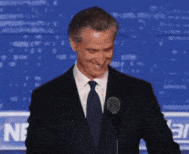 a man in a suit and tie smiles while standing in front of a microphone in front of a sign that says ne 37