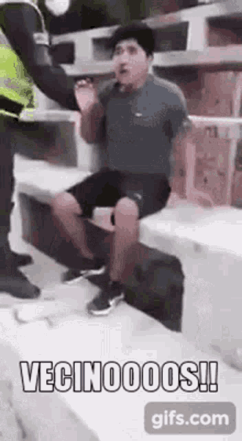a man is sitting on a bench while a police officer holds his hand over his head .