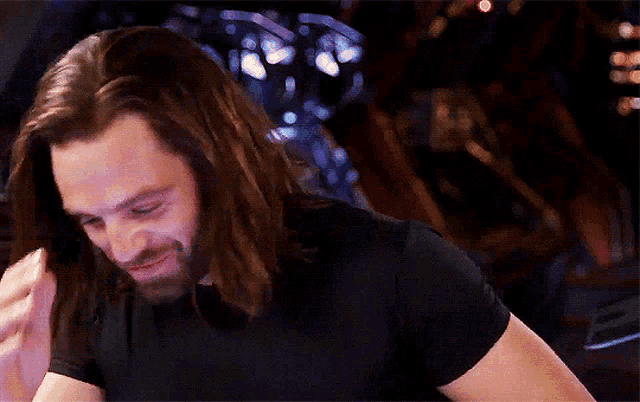 a man with long hair and a beard is holding his hand to his head .