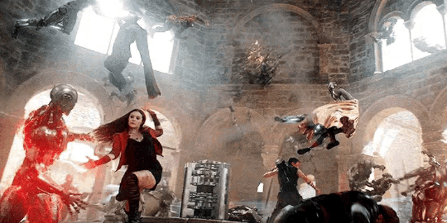a woman in a red jacket is standing in a room with a bunch of superheros .