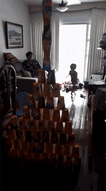 a woman sits on a couch in a living room while a boy plays with a tower made of cups