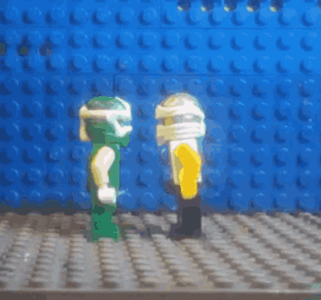 two lego figures are standing next to each other in front of a blue brick wall