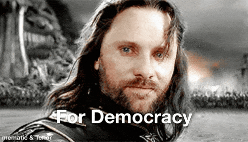 a man with long hair and a beard is looking at the camera with the words `` for democracy '' written above him .