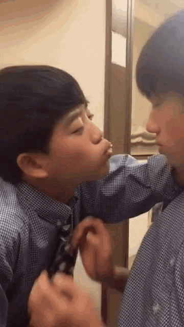 a boy is kissing another boy on the cheek in front of a mirror