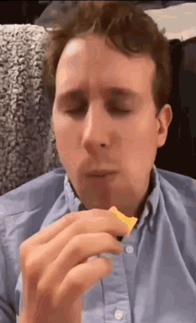 a man in a blue shirt is eating a piece of food with his eyes closed