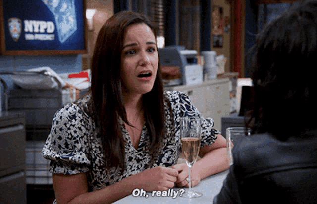 a woman is sitting at a table with a glass of champagne and says " oh really "