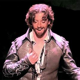 a man with a beard is wearing a leather jacket and taking off his shirt