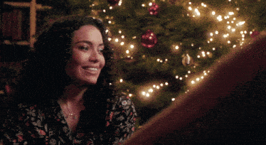 a man and woman sit in front of a fireplace with a christmas tree in the background
