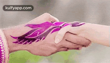 a man is holding a woman 's hand with a purple tattoo on his hand .