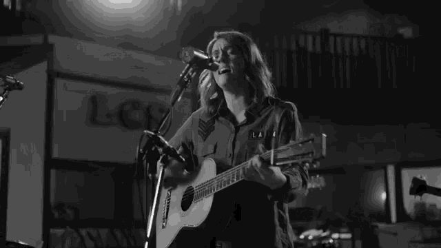 a woman is singing into a microphone while holding a guitar