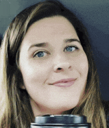 a woman with long hair is smiling and holding a cup of coffee