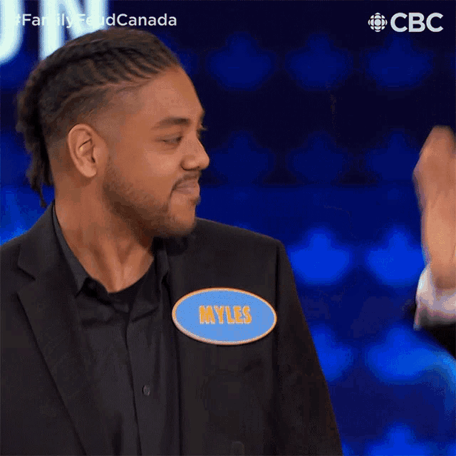 a man in a suit is standing in front of a blue background with a cbc logo