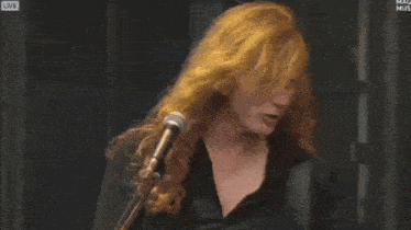 a man with long red hair is singing into a microphone while another man plays a guitar