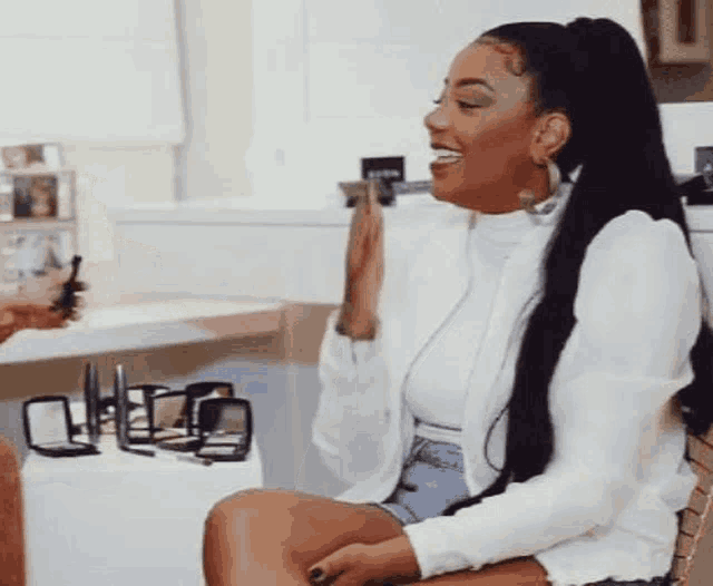 a woman is sitting in a chair in front of a table with a lot of makeup on it .