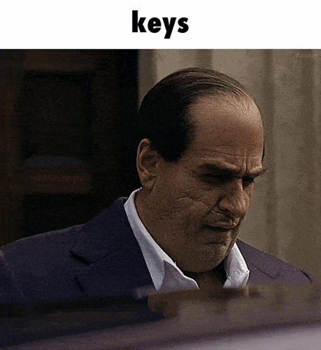 a man in a suit and white shirt is looking down with the word keys above him