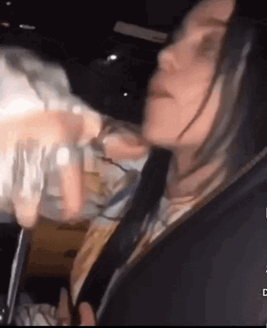 a woman is sitting in a car holding a glass of water .