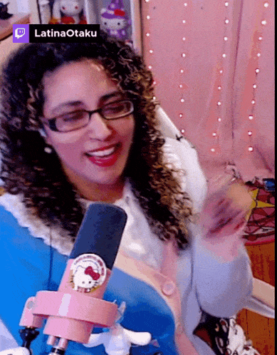 a woman wearing glasses and a hello kitty pin is smiling in front of a microphone