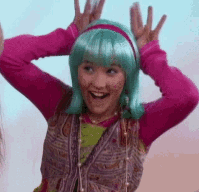 a girl wearing a pink shirt and a green wig is making a funny face