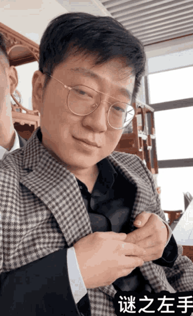 a man wearing glasses and a plaid jacket has chinese writing on his sleeve