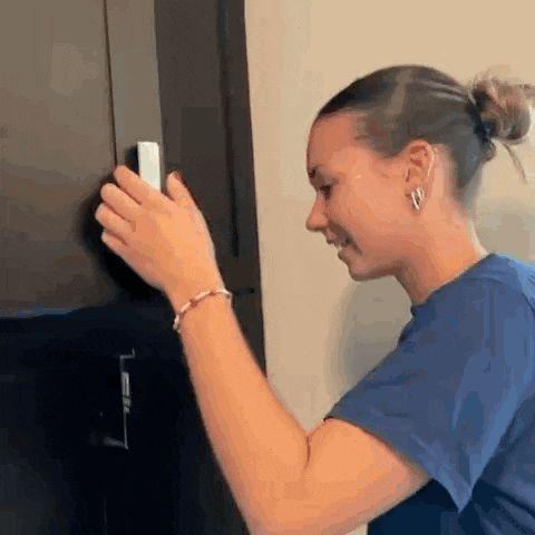 a woman is holding a remote control in her hand while standing next to a door .