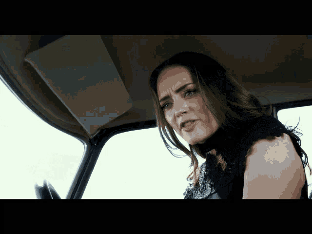 a woman in a black top is sitting in a car and making a funny face