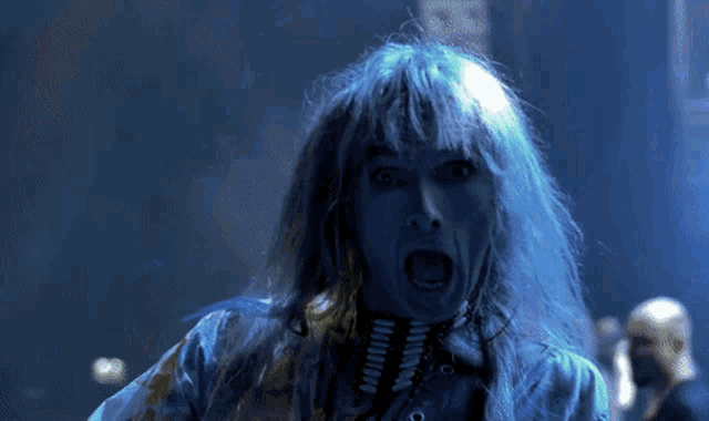 a man with blue hair is screaming and looking at the camera