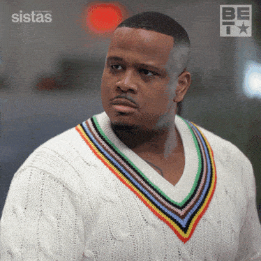 a man wearing a white sweater with a rainbow colored v-neck is standing in front of a poster for sistas