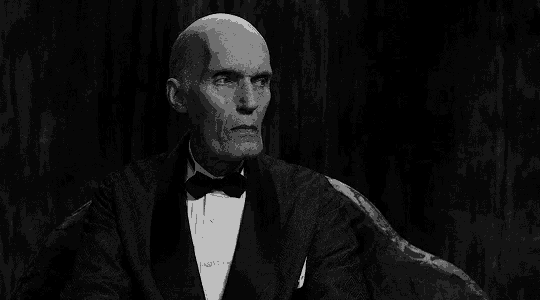 a black and white photo of a bald man in a tuxedo and bow tie .