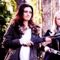 a woman in a fur coat is holding a gun next to another woman .